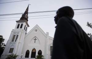 The steeple of Emanuel African Methodist Episcopal Church stands as a pedestrian passes early Sunday, June 21, 2015, in Charleston, S.C. Members of a historic black church in the U.S. will return to their sanctuary Sunday and worship less than a week after a white gunman killed nine people there, and similar sermons of recovery and healing will reverberate throughout the country. (AP Photo/David Goldman)